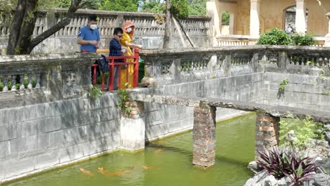 Young-boy-and-his-parents-feeding-Koi-Fish-in-pond-at-Hue,-Vietnam