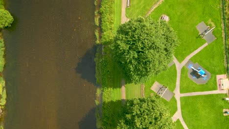 Aerial-Drone-shot-overflying-a-river-beside-a-park-with-trees