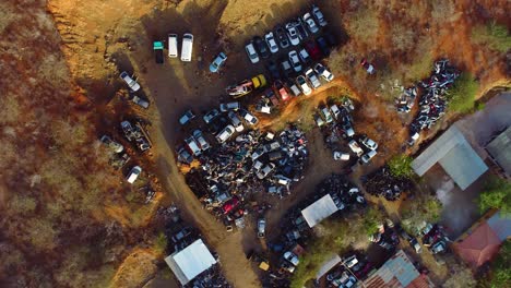 4k-top-down-drone-riser-with-slow-spin-of-a-backyard-car-scrapyard-in-a-Caribbean-neighborhood-during-golden-hour