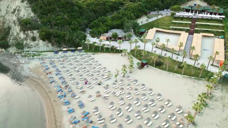 Beach-by-the-Adriatic-Sea,-umbrellas,-sunbeds,-and-restaurant-buildings,-aerial-view-from-a-drone