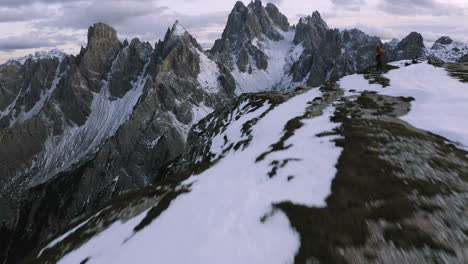Snowy-Cadini-di-Misurina-and-hikers-on-a-mountain-ridge,-dusk-in-Dolomites,-Italy---reverse,-drone-shot