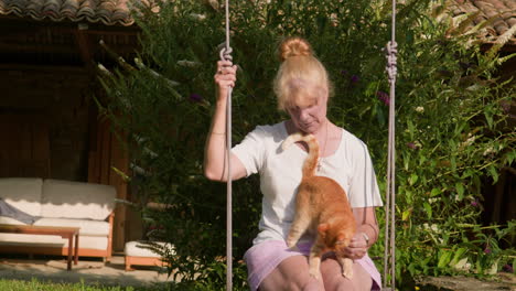 Cute-ginger-cat-enjoys-tender-love-and-care-from-woman-on-garden-swing-slow-mo
