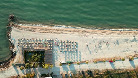 Albania,-drone-view-of-the-emerald-waters-of-the-Ionian-Sea-and-the-beach-with-umbrellas-and-sunbeds