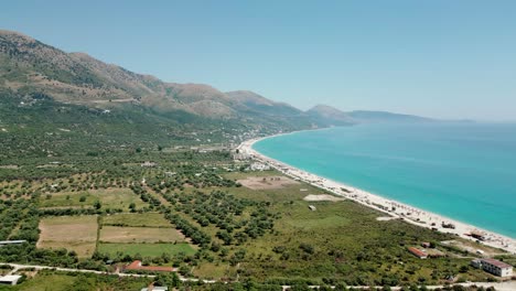 Albania,-drone-view-of-the-beach,-emerald-waters-of-the-Ionian-Sea,-and-the-Ceraunian-Mountains
