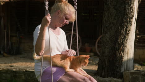 Cute-ginger-cat-enjoys-love-and-attention-from-woman-on-garden-swing-slow-mo