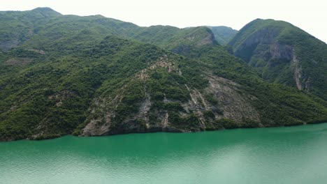 Albania,-Lake-Koman-amidst-the-Accursed-Mountains,-a-boat-sailing-on-emerald-waters
