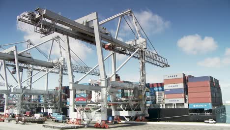 White-container-cranes-loading-vessel-on-cargo-harbour,-sunny-summer-day
