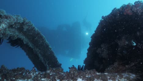 A-scuba-diver-exploring-a-deep-artificial-wonder-reef-structure-using-underwater-lights