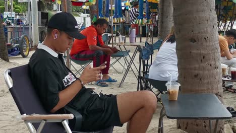 Thai-Boy-Enjoying-Coffee-and-Technology:-Relaxing-on-a-Beach-Chair-with-Smartphone