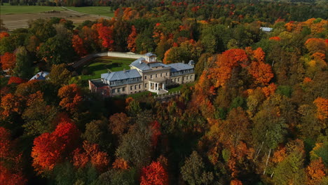 Aerial-drone-view-of-a-beautifully-modern-country-house-surrounded-by-gorgeous-trees-at-peak-color-and-a-beautiful-forest-landscape-as-the-drone-fly-away---Colorful-autmn