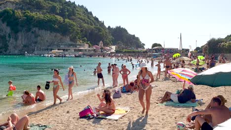 Gente-En-La-Playa-Nadando-Y-Tomando-El-Sol,-Hermosas-Chicas-Caminando-Sobre-La-Arena,-Palaiokastritsa-Corfu-Kerkyra-Grecia,-Imágenes-En-Tiempo-Real