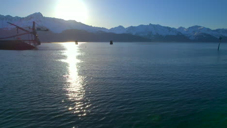 Drone-flying-over-water-towards-mountains-and-sunrise-in-Seward-Alaska