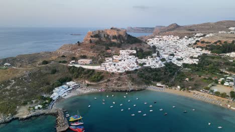 Aerial-footage-of-Lindos-beach,-the-Acropolis-of-Lindos-above-Lindos-town-at-sunrise