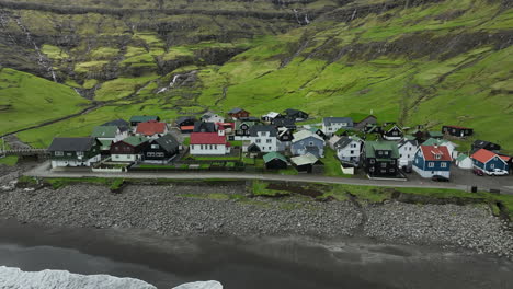 Tjørnuvík-village,-Faroe-Islands:-close-up-aerial-view-traveling-in-to-the-pretty-village,-with-the-ocean-and-mountains-in-the-background