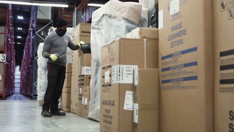 A-BIPOC-Ashley-Furniture-HomeStore-warehouse-merchandise-worker-checks-a-line-of-cardboard-boxes-inside-a-Canadian-distribution-center