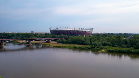 Aerial-establishing-shot-of-Vistula-River-with-bridge-and-famous-Warsaw-Narodowy-Stadium,-Poland