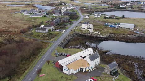 Reversing-and-tilting-wide-angle-drone-shot-featuring-the-Taigh-Chearsabhagh-building-as-well-as-the-moor,-peatland,-mountains-and-lochs-around-Lochmaddy-on-the-Isle-of-North-Uist,-Hebrides