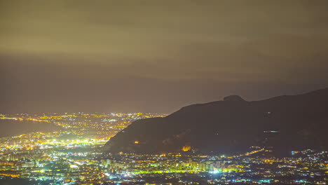Misty-nighttime-city-lights,-viewed-from-a-hill-in-Sicily,-Italy