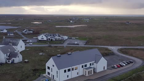 Reversing-drone-shot-of-the-village-of-Daliburgh-and-the-Cnoc-Soilleir-building-in-South-Uist,-part-of-the-Outer-Hebrides-of-Scotland