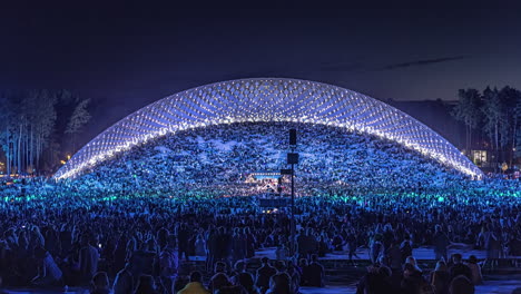 Timelapse-shot-of-huge-crowd-enjoying-beautiful-light-show-at-Latvian-Song-and-Dance-Festival-in-an-outdoor-stadium-in-Riga,-Latvia-during-evening-time
