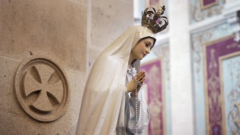 Statue-of-Virgin-Mary-with-white-dress-and-rosary-in-hands,-inside-church