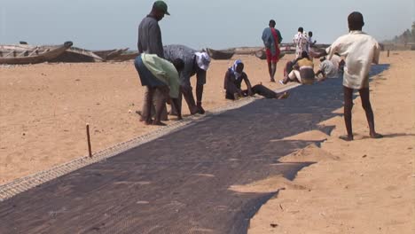Gruppe-Nigerianischer-Fischer,-Die-Ihr-Netz-Am-Strand-Reparieren