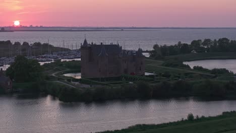 Side-panning-shot-of-medieval-fortress-Muiderslot-castle-at-Muiden-with-sunset,-aerial