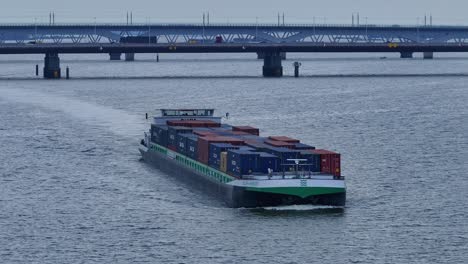 Grün-weißes-Containerschiff,-Das-Sich-Auf-Einem-Fluss-In-Den-Niederlanden-Bewegt,-Mit-Brücken-Im-Hintergrund