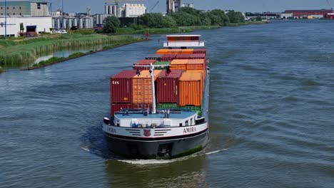 Ein-Amira-Frachtschiff,-Das-Container-Auf-Einem-Fluss-Transportiert,-Mit-Stadtgebäuden-Im-Hintergrund