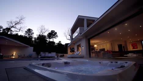 Beautiful-modern-mansion-with-steaming-hot-jacuzzi-at-blue-hour-with-the-lights-on
