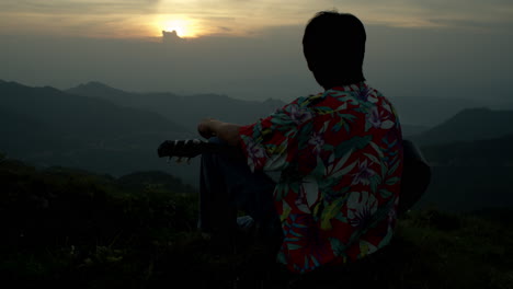 Guitar-Player-Looks-at-the-Sunset-with-Sunglasses-at-Mountain-Top-Southeast-Asia-Wearing-Vintage-Colorful-Shirt