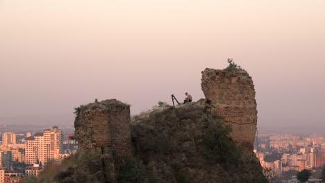 Adventurous-man-climbing-on-ruin-with-view-over-tbilisi-at-sunset