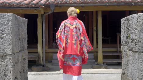 Una-Mujer-Recibiendo-Una-Casa-Tradicional-Japonesa-En-El-Mundo-De-Okinawa,-Naha,-Japón,-Vistiendo-Un-Vestido-De-Kimono-Ryusou,-Un-Día-Caluroso-De-Verano,-Una-Casa-De-Piedra-De-Madera,-Bájese-De-Los-Zapatos-Geta.