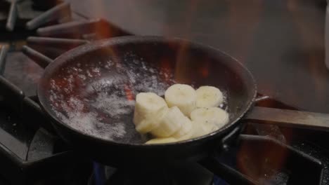 Pouring-liquid-into-a-pan-of-Bananas-cooking-with-fire