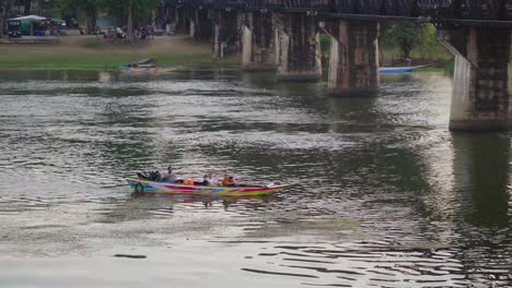 A-group-of-tourists-returning-from-a-speedboat-ride-along-the-Khwae-river,-passing-under-the-famous-Kwai-river-bridge,-Kanchanaburi,-Thailand