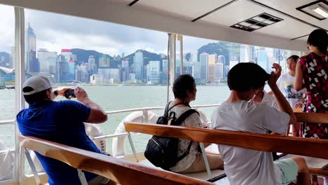 Tourists-Crossing-Victoria-Harbour-on-the-Star-Ferry,-Taking-Pictures-of-Skyline