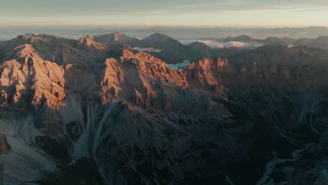 Drone-footage-pushing-in-towards-the-stunning-Punta-Sud-di-Fanes,-Punta-Nord-and-Monte-Ciaval-mountain-peaks-in-the-Dolomites-of-Cortina-D'Ampezzo,-Italy-at-sunrise