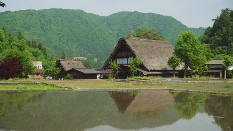 Reflection-of-giant-house-with-thatched-roof-and-mountains-full-of-greenery,-ponds-for-planting-Shirakawago-Japan