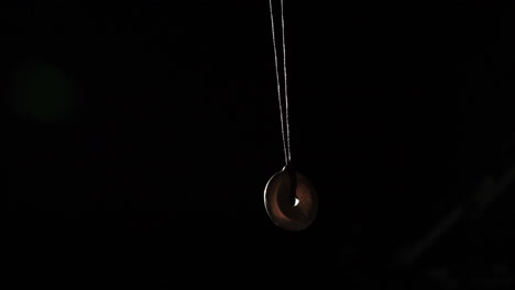 Pendulum-used-for-hypnotism-and-readings-swinging-against-black-background