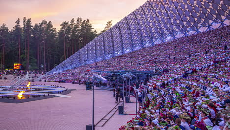 A-crowd-of-singers-and-performers-sit-in-the-stadium-stage-and-sing-during-the-Latvian-Song-and-Dance-Festival