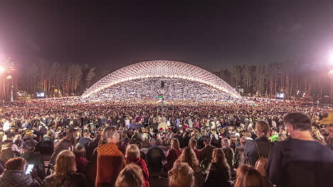 Timelapse-shot-of-huge-crowd-of-locals-enjoying-Latvian-Song-and-Dance-Festival-in-an-outdoor-stadium-in-Riga,-Latvia-after-sunset
