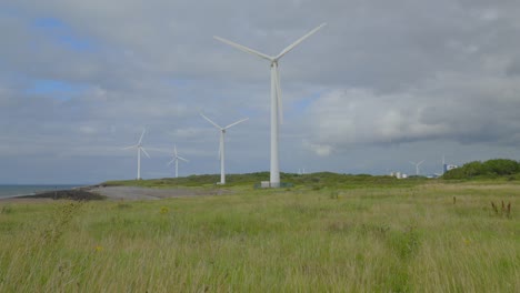 Windmills-rotating-through-yellowed-grasses-with-rise-up-clearing-grass-showing-cloudy-summer-sky