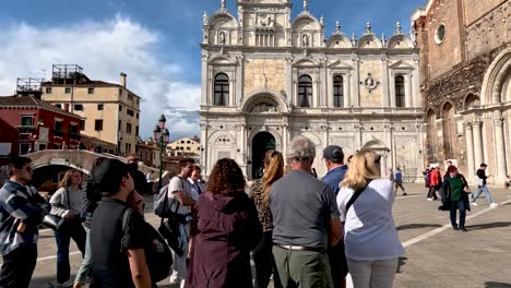 Group-Of-Tourists-Standing-In-Piazza-Outside-San-Zanipolo-Church-And-Scuola-Grande-di-San-Marco-In-Venice-On-Sunny-Day-In-May