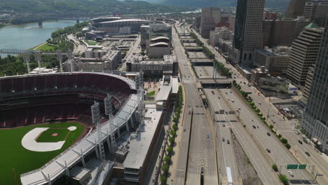 Reverse-aerial-reveal-of-downtown-Cincinnati,-the-stadiums,-and-traffic