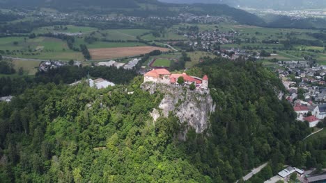 Cinematic-drone-shot-of-Castle-build-on-green-hill-in-Bled-City,-during-cloudy-and-sunny-day,-Slovenia---Orbiting-shot