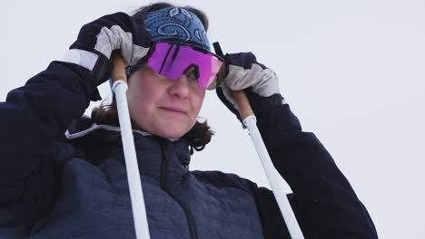 Orbiting-slow-motion-low-angle-shot-of-female-skiier-taking-down-goggles