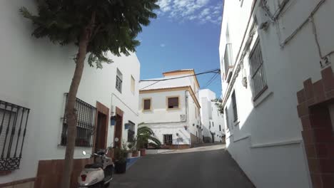 A-view-of-a-narrow-street-in-a-Spanish-white-village-with-a-lone-scooter-parked,-pan