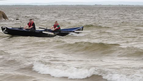 Strong-pair-of-men-row-vigorously-through-open-ocean-in-currach-boat