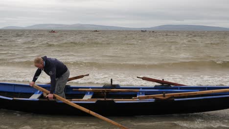 Man-walks-along-inside-of-traditional-irish-currach-boat-adjusting-wooden-oars