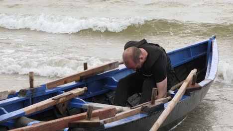Man-inspects-hull-of-currach-boat-stretching-and-using-sponge-to-remove-water